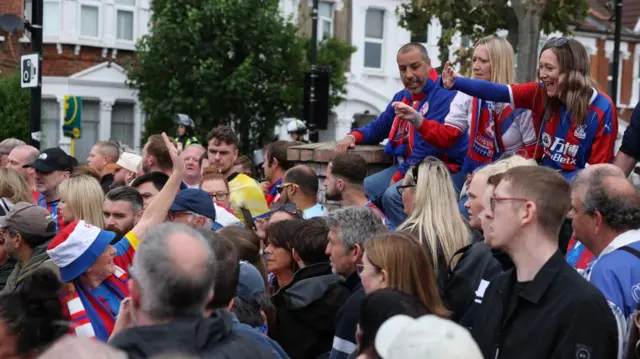 A crowd of people with three sat above them in Crystal Palace tops