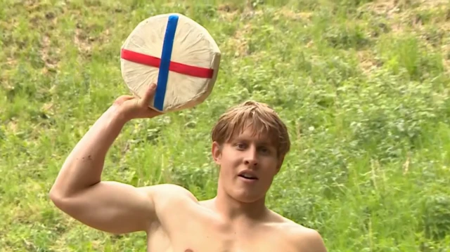 Tom Kopke shirtless hold up a wheel of Double Gloucester cheese after winning