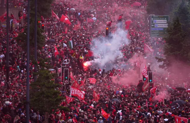 Crowd of LIverpool supporters await the team bus, as some wave red flags and others let off red flares