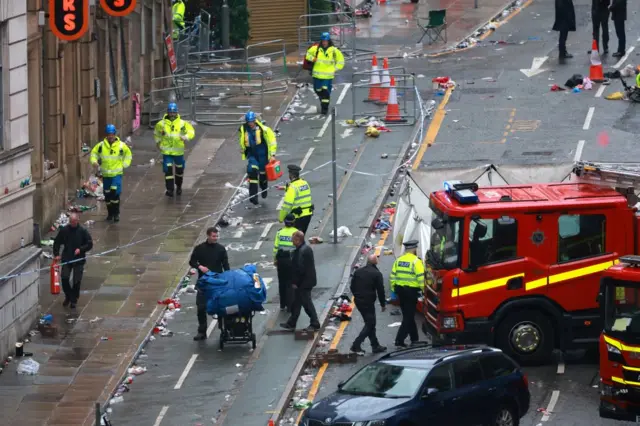 Police and emergency services surround a fire engine on an empty street filled with rubbish