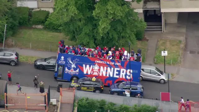 A bus driving packed with people on the top of it. It says winners on the side