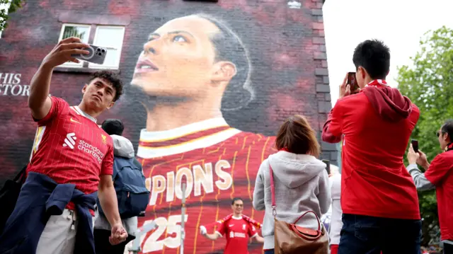 Liverpool fans take selfies in front of a wall mural of Virgil Van Dijk