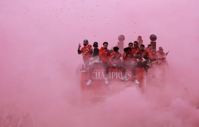 Liverpool players on the top of a bus in a cloud of red smoke