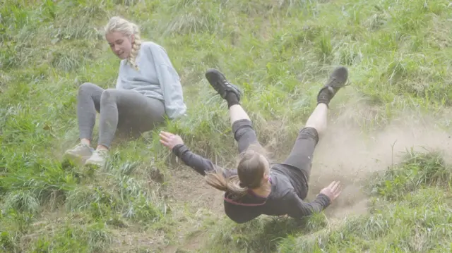 Two women are coming down the hill with dust coming up around them.