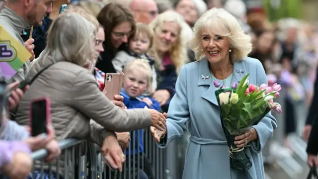 Queen Camilla shaking hands with a member of the public, holding a bunch of tulips