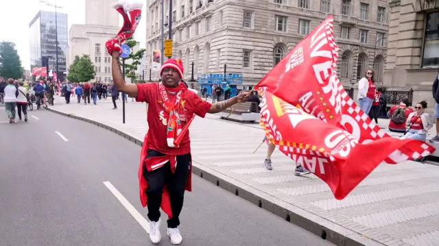 Liverpool fan in red shirt, hat and scarf waves a Liverpool flag