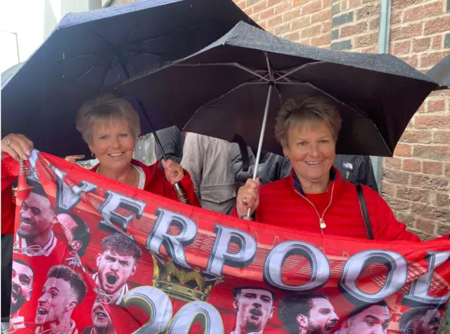 Twins Di and Adele dressed in red and holding a Liverpool banner