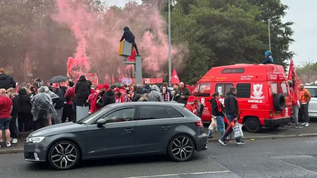 Crowds in the road with red flares and an LFC branded van
