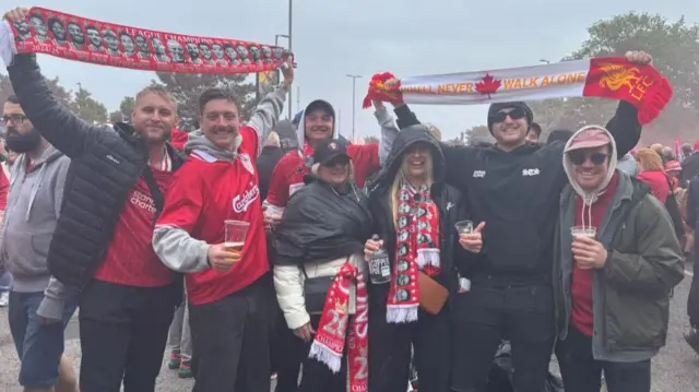Group of people wearing Liverpool shirts and holding flags