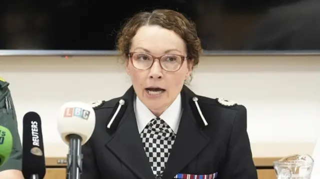 Police officer giving a press conference, there are several microphones in front of her