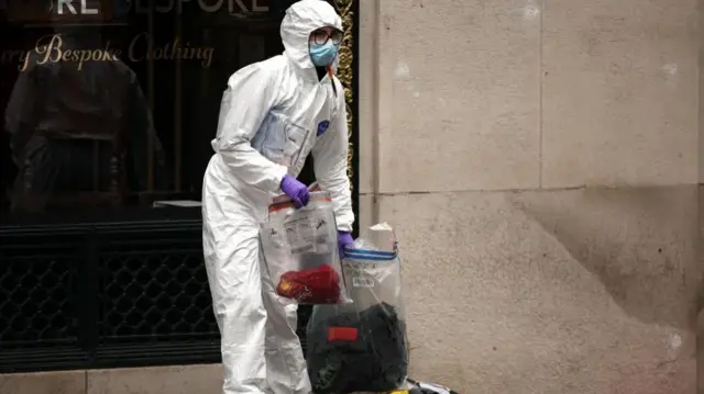 Forensics worker in PPE holding a see through bag with a Liverpool shirt in it