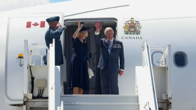 Queen Camilla and King Charles waving outside the plane door