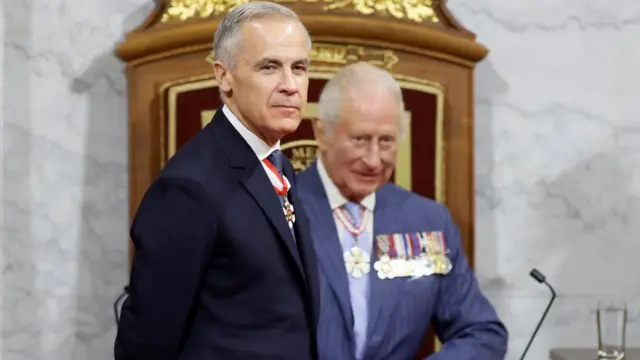 Carney smiles as he stands in the foreground in front of Charles, who sits on the throne