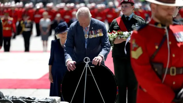 King Charles lays a wreath onto a thin white frame at the memorial