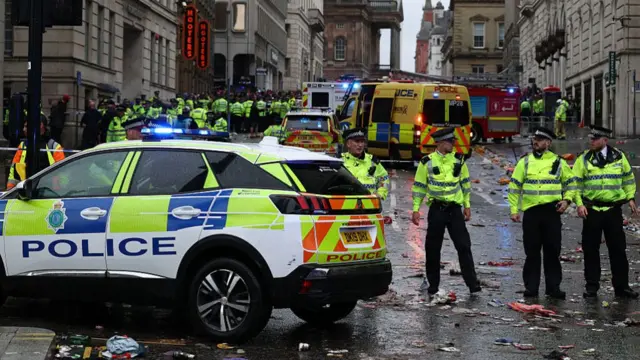 A large police presence at the scene shortly after the incident took place. A fire truck and ambulance are in the street, as are large numbers of police officers