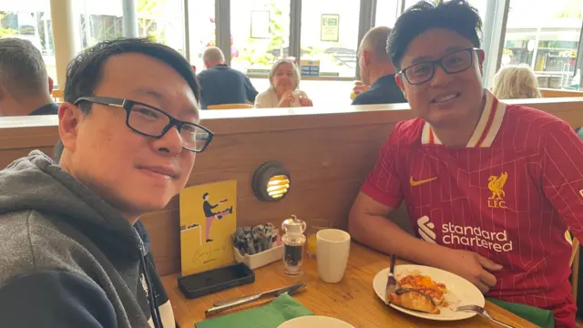 Two men sit at a table eating food.