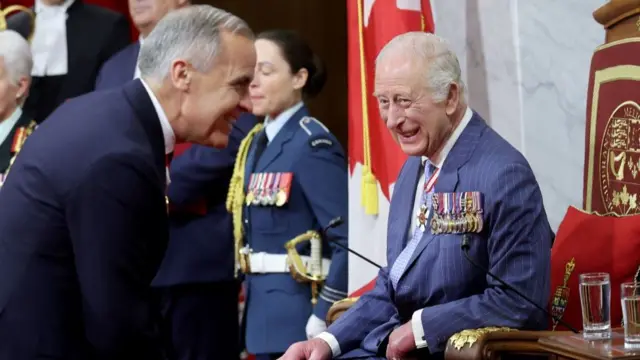 Mark Carney and King Charles laughing together as the King sits on the throne