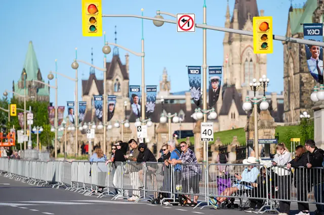 Members of the public wait behind street barriers