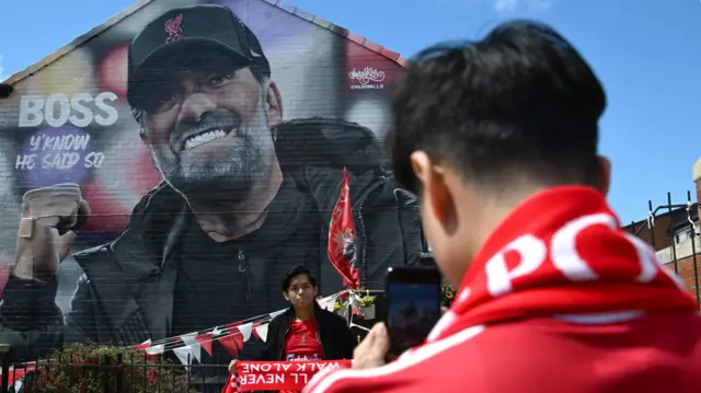 Liverpool fans pose for a photo in front of a mural of former Liverpool manager Jurgen Klopp the Premier League match at Anfield, Liverpool.