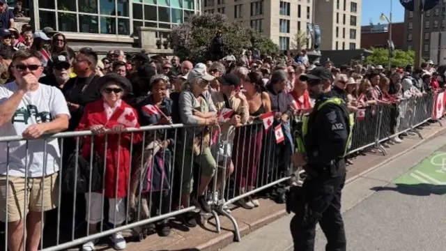 Spectators stand behind a rail as they wait for the Royal procession