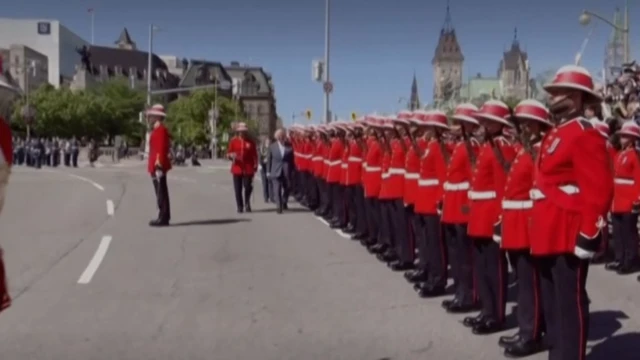 A wider view of Charles walking alongside Mounties in red coats lined up on a street