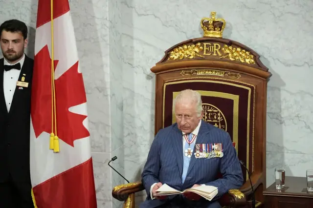 The King reads his speech on the throne next to the Canadian flag