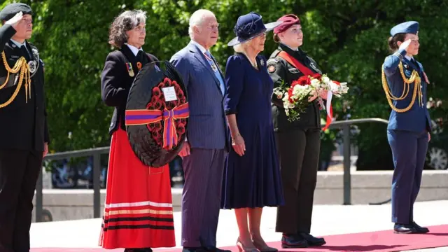 Charles and Camilla stand beside two people holding wreaths