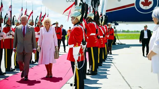 Royals walking on a red carpet after getting off a plane. They are greeted by Canadian soldiers.