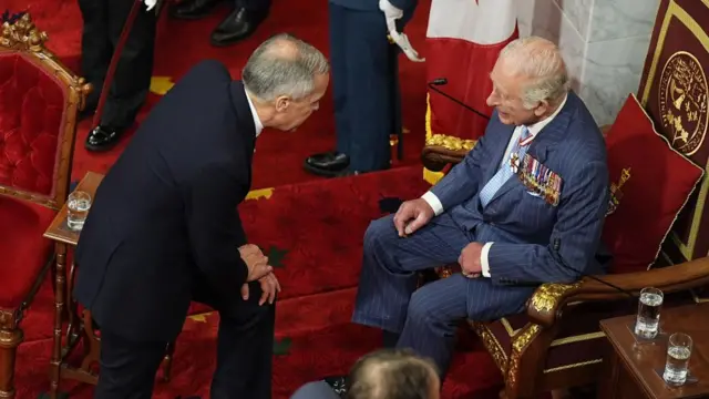 Charles, sitting on the throne, smiles as Carney leans forward to speak to him