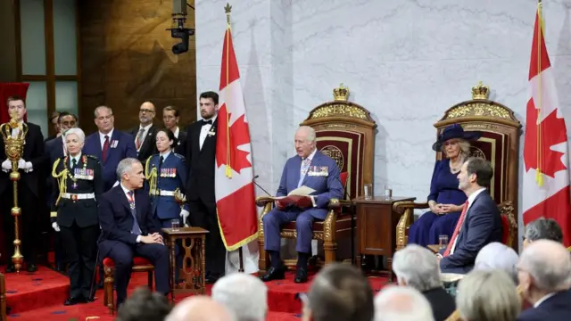 King, seated, reads speech in Canada's Senate. Carney and Queen Camilla look on.