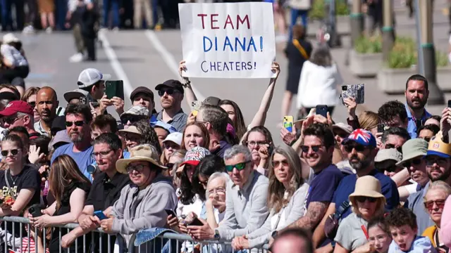 A member of the crowd holds a sign which says 'Team Diana! Cheaters!'