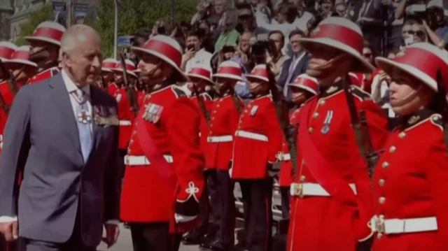 Charles walks alongside Mounties in red coats lined up