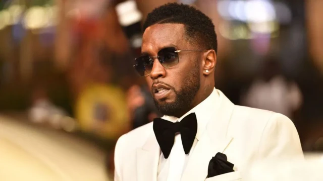 A photograph of Diddy, who wears a white suit and sunglasses