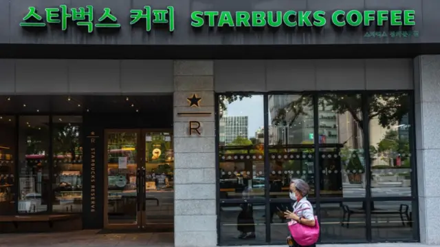 A woman with short hair and a pink handbag walks past a Starbucks store in South Korea