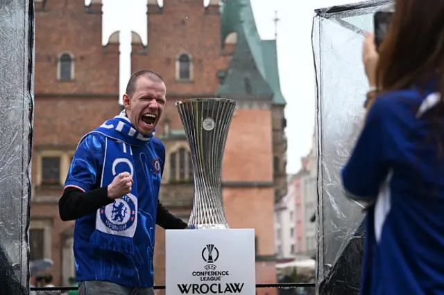 A Chelsea fan poses for a photo with the UEFA Conference League trophy