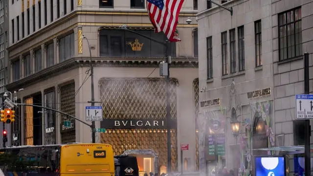 The United States flag flies in front of a Bulgari store on 5th Avenue in New York City. A bus with a yellow back is in the background
