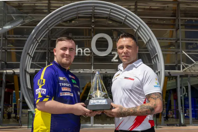 Luke Littler and Gerwyn Price holding the Premier League Darts trophy