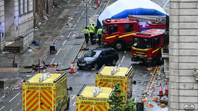 Three parked ambulances and two fire trucks stand on Water Street as three police officers observe the scenes of the crash. The street is covered in litter after the parace