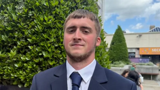 Headshot of Kian sitting in front of a tree with his mouth pushed shut