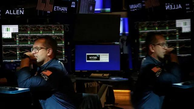 NYSE trader sits at a computer. he is reflected on screens nearby