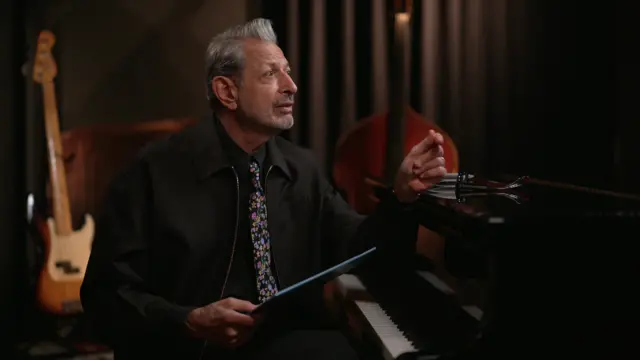 Jeff Goldblum in a room with a guitar and cello in the background