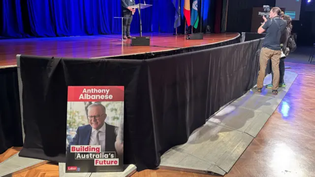 A poster of Albanese is perched on the ground in front of a stage.