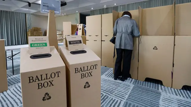 A woman in a grey shirt filling out her ballot slip at the polling booth.