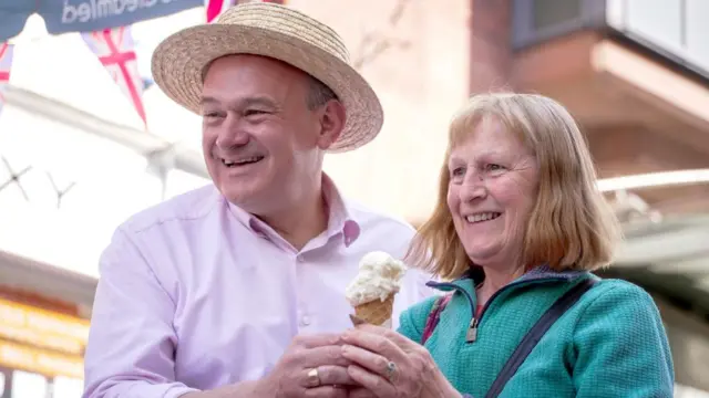 Ed Davey stands next to a woman - they both hold an ice cream as they pose to the camera