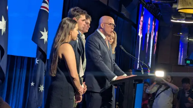 Dutton speaking at a podium on stage, surrounded by his family