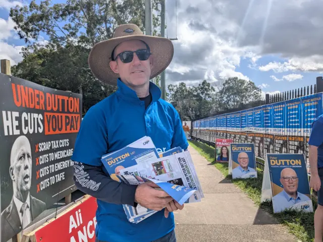 Kenneth King, a volunteer for Peter Dutton's campaign, holds pamphlets in front of election posters