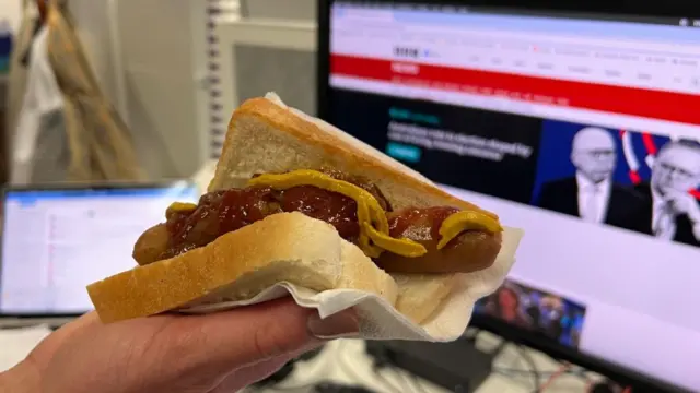 A photo of a sausage on a single slice of white bread with onions, mustard and tomato sauce.