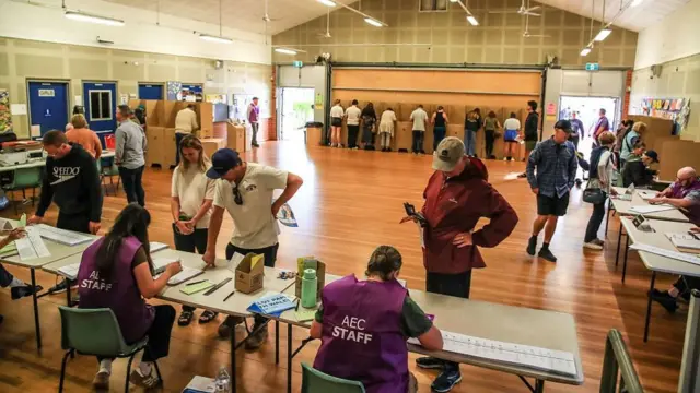 People voting at a polling station in Newcastle, Australia.  Photo shows Australian Electoral Commission in purple tabards marking attendance.