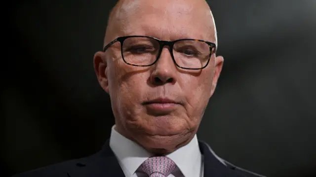 Opposition Leader Peter Dutton looks down during a press conference in the electorate of Tangney and suburb of Myaree on May 02, 2025 in Perth, Australia. He is only visible neck up and is wearing a white shirt, black blazer and pale pink tie with a print on it.
