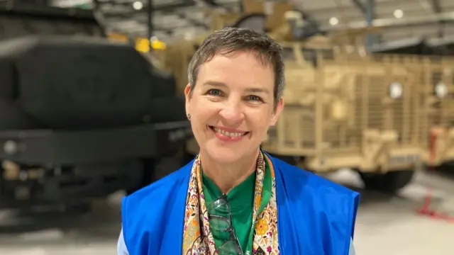Headshot of woman with short hair smiling in front of two parked trucks in a warehouse